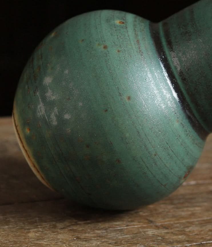 Small sage green vase for flowers, textured ceramic, on rustic wood.